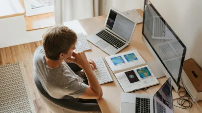 High-Angle Shot of a Boy Sitting on Grey Chair while Using His Laptop Computers